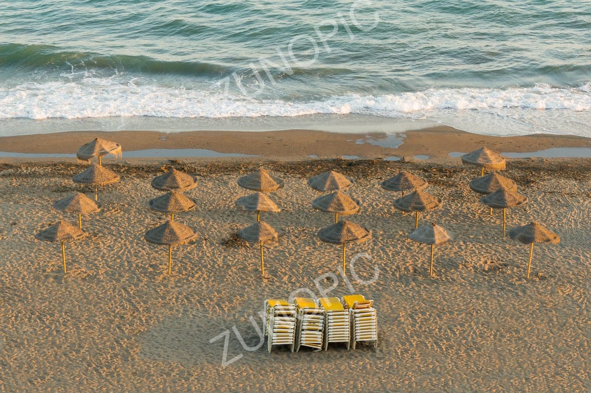 Rows of thatched beach umbrellas on an empty sandy beach at dusk