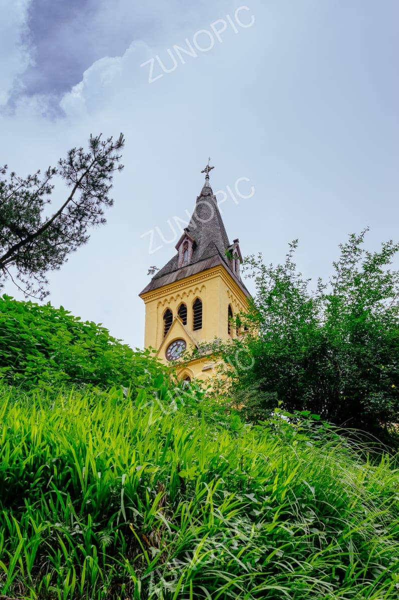 Yellow church tower rising above green hillside grass