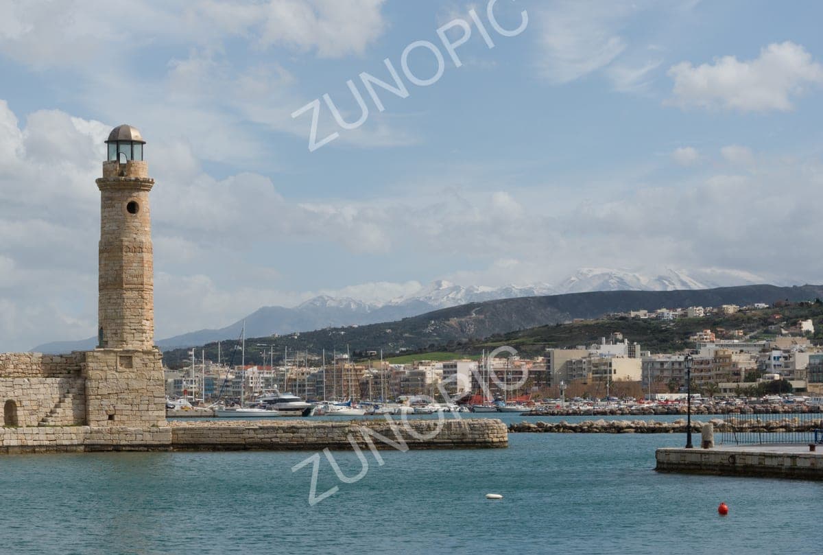 Old Venetian lighthouse at a harbour entrance with snowy mountains