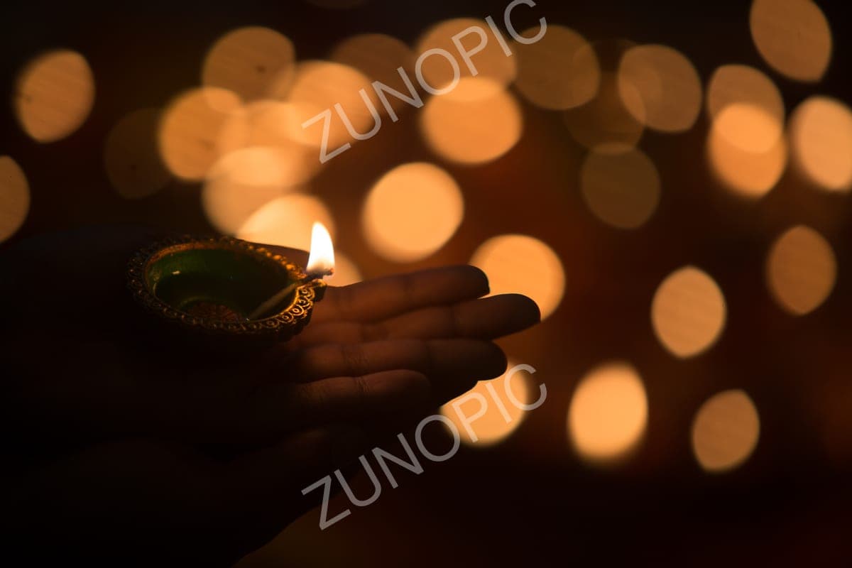 Hand holding a lit diya against golden bokeh
