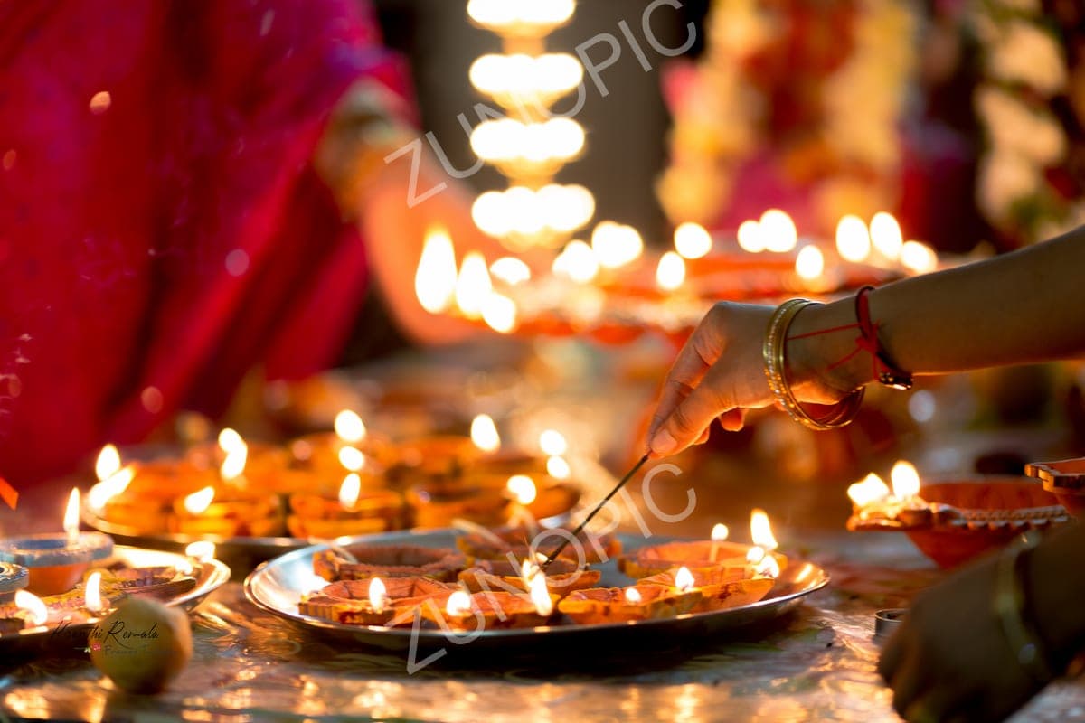 Women lighting diyas on brass plates for a festival