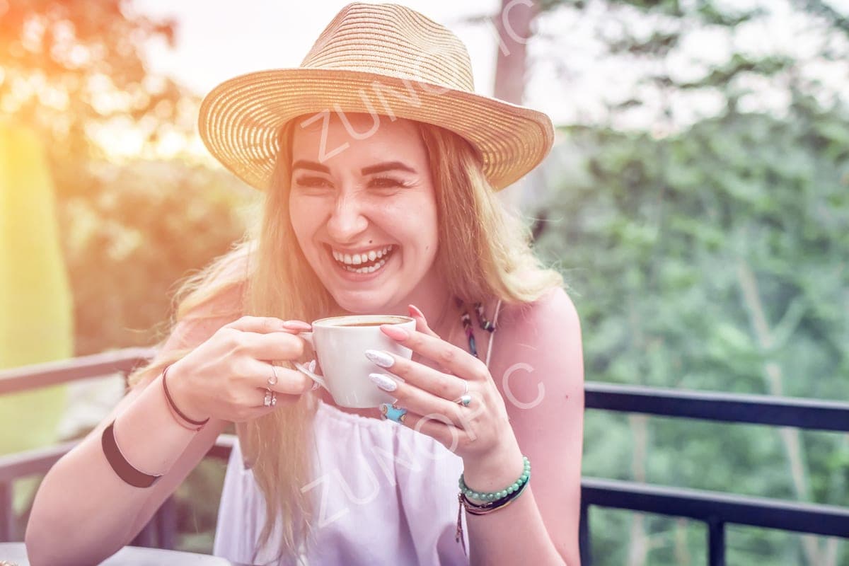 Laughing woman in a straw hat holding a coffee cup